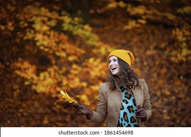 Hello autumn. happy young female in brown coat and yellow hat with autumn yellow leaves outdoors on the city park in autumn.