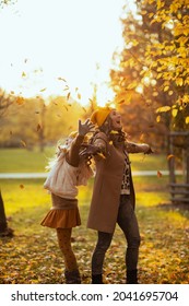 Hello Autumn. Happy Young Mother And Child In Orange Hats Outside In The City Park In Autumn Throws Up Autumn Leaves.