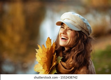 Hello Autumn. Portrait Of Happy Elegant 40 Year Old Woman In Sweater, Hat, Gloves And Scarf With Yellow Leaves Enjoy Autumn Time While Sitting On A Bench Outside In The Autumn Park.