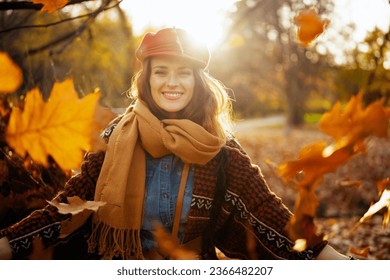 Hello autumn. Portrait of happy elegant female in red hat with scarf throwing autumn leafs in the city park.