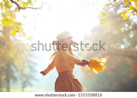 Hello autumn. smiling young woman in sweater, skirt, hat, gloves and scarf with yellow leaves having fun time outside in the autumn park.
