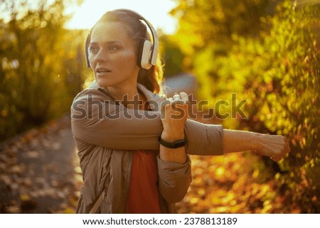 Hello autumn. stylish 40 years old woman in fitness clothes in the park with headphones stretching.