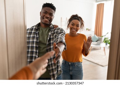 Hello. Cheerful Black Spouses Stretching Hands For Handshake Smiling To Camera Meeting Somebody Standing Near Opened Door At Home. Nice To Meet You, Welcome To Our House Concept. Selective Focus