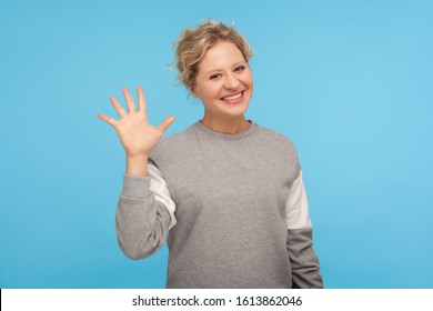 Hello! Cheerful woman with short hair in casual sweatshirt smiling friendly at camera and waving hi, welcoming or showing goodbye, hospitable greeting. indoor studio shot isolated on blue background - Powered by Shutterstock