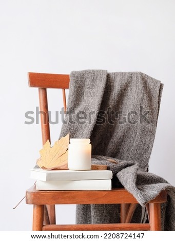 Hello fall. Cozy warm image. Candle mockup design. Cozy interior with old vintage chair, warm plaid, books and autumn leaves. Burning candle mockup design