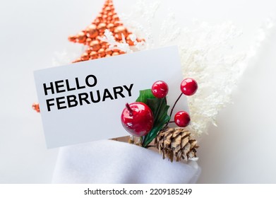 Hello February Text On A Card Next To Christmas Decorations On A White Background