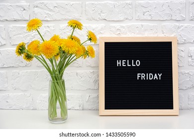 Hello Friday words on black letter board and bouquet of yellow dandelions flowers on table against white brick wall. Concept Happy Friday. Template for postcard.