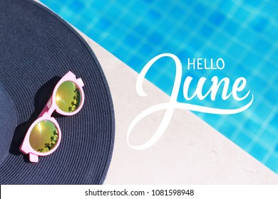 Hello June hand lettering, sun hat and sun glasses near the swimming pool.