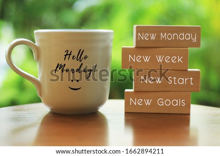 Hello Monday concept with inspirational quote on wooden blocks - New Monday. New Week, New Start. New Goals. And a smiling face on a white morning cup of coffee or tea.