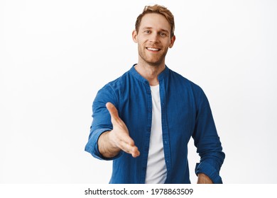 Hello nice to meet you. Smiling handsome redhead man extend hand for handshake, look friendly, greet you, hi gesture, standing over white background