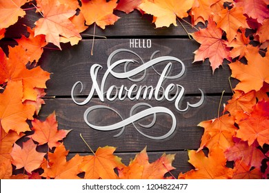 Hello November hand lettering inscription with orange and red maple leaves frame on old wooden background. Autumn decor, fall mood.