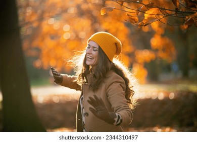 Hello november. smiling stylish woman in brown coat and yellow hat dancing outside on the city park in autumn. - Powered by Shutterstock