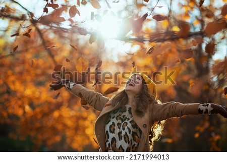 Hello november. smiling trendy 40 years old woman in beige coat and orange hat rejoicing outside in the city park in autumn.