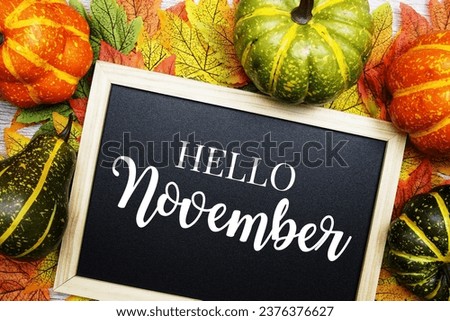 Hello November text on blackboard decorated with maple leaves on wooden background
