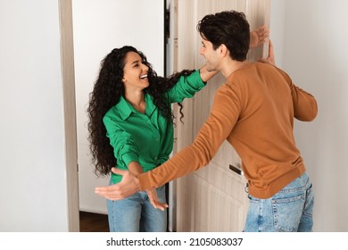Hello. Portrait of cheerful happy young woman greeting man while meeting him at front door, hugging and inviting male visitor to enter apartment, welcoming friend home, couple standing in doorway