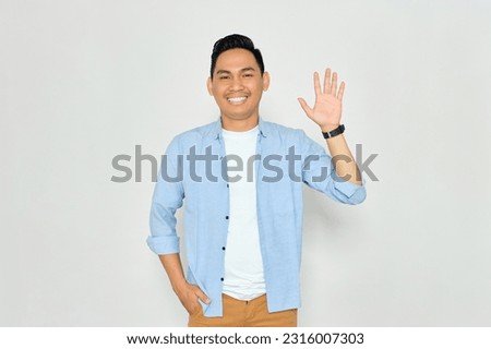 Hello. Portrait of friendly young Asian man in casual clothes showing hi gesture with waving hand and smiling isolated on white background