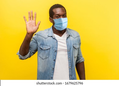 Hello! Portrait of positive handsome man with medical mask with rolled up sleeves smiling friendly and waving hand saying hi, welcoming gesture. indoor studio shot isolated on yellow background