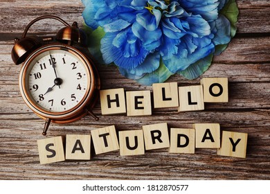 Hello Saturday Alphabet Letters With Alarm Clock And Blue Flower On Wooden Background