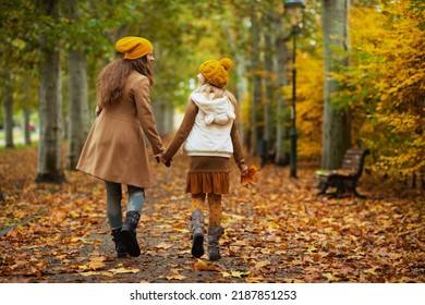 Hello September. Seen From Behind Young Mother And Child In Yellow Hats With Autumn Yellow Leaves Walking Outside On The City Park In Autumn.