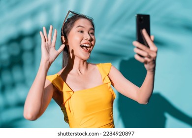 hello summer asia woman influencer in swimwear positive photo selfie using smartphone hand gesture action photo shoot with smile and happiness in summertime studio shot on blue colour background - Shutterstock ID 2284920897