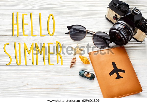 hello summer text, travel\
and wanderlust concept, summer vacation, space for text. photo\
camera sunglasses passport  car shells on white wooden table.\
planning  holiday