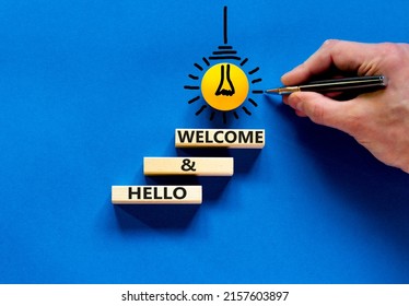 Hello And Welcome Symbol. Concept Words Hello And Welcome On Wooden Blocks. Businessman Hand. Yellow Light Bulb Icon. Beautiful Blue Background. Business Hello And Welcome Concept. Copy Space.