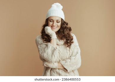 Hola invierno. una mujer alegre y elegante con suéter beige, mitones y sombrero aislado en el fondo beige.