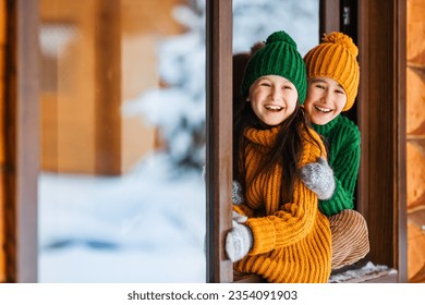 Hello winter holiday! Happy children play together outdoor in open window. Happy New Year and Merry Christmas family celebration!