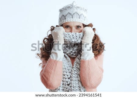 Hello winter. stylish middle aged woman in sweater, mittens, hat and scarf wrapping up in a scarf isolated on white.