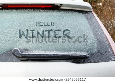 Hello winter word text on frozen back window of car. Snow on window of parking white car in winter day. 