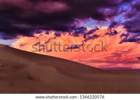 Hell-red stormy clouds in the sky over deserted sand dunes on Australian coast of Pacific ocean during storm weather at sunset.