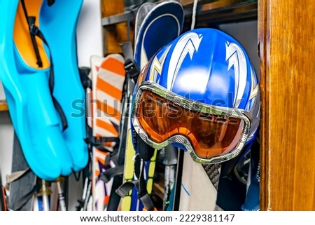 Helmet, ski mask, ski hanged on customized wooden wall mount at warehouse for seasonal storage at ski resort. Extreme winter sport equipment handling at home