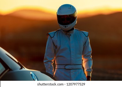 A Helmet Wearing Race Car Driver In The Early Morning Sun Looking At His Car Before Starting