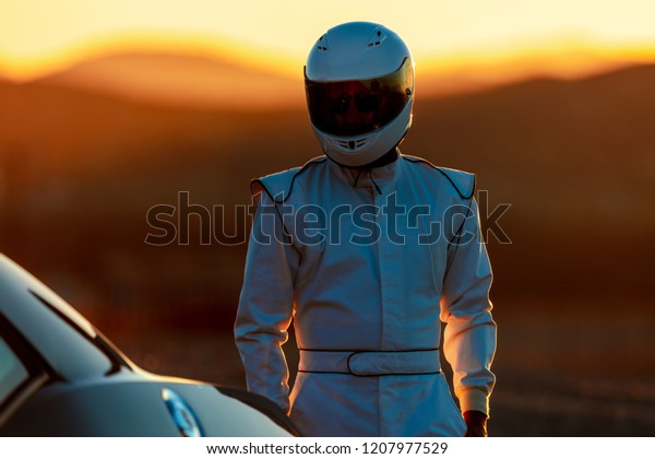 A Helmet Wearing Race Car Driver\
In The Early Morning Sun Looking At His Car Before\
Starting