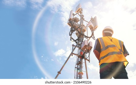 Helmeted asian male engineer works in the field with a telecommunication tower that controls cellular electrical installations to inspect and maintain 5G networks installed on high-rise buildings.