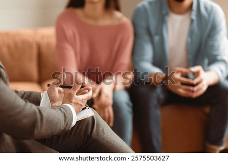 Help Concept. Closeup Cropped View Of Man Counselor Therapist Or Consultant In Suit Talking With Couple Sitting In Office, Giving Professional Advice. Selective Focus On Hands With Clipboard And Pen
