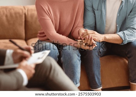 Help Concept. Closeup Cropped View Of Spouses Having Session With Man Marriage Therapist, Sitting On Couch In Office And Holding Each Other Hands. Consultant Writing Taking Notes, Selective Focus
