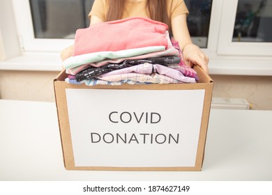 Help With Coronavirus Covid 19. A Volunteer Girl At A Charity Center Holds A Box Of Donation Clothing