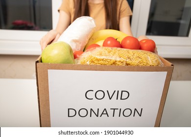 Help With Coronavirus Covid 19. A Volunteer Girl At A Charity Center Holds A Box Of Donation Food Products 