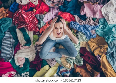 Help. High angle above view photo of stressed yelling lady stay home spring, cleaning household sit many clothes stack floor pick select look outfit nothing to wear hands on head indoors