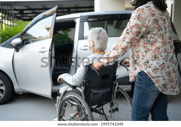 Help and support asian senior or elderly old\
lady woman patient sitting on wheelchair prepare get to her car,\
healthy strong medical\
concept.
