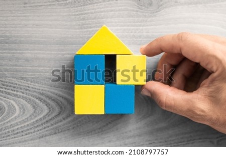 Help support build Ukraine concept. Refugee housing. Ukraine flag colors. Hand putting together home shape puzzle