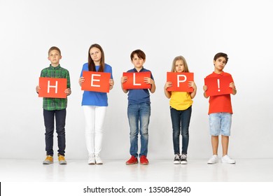 Help Warms The Heart. Group Of Sad Serious Children Or Teenagers With Red Banners Making Word Isolated On Studio Background. Education, Advertising And Social Rights Concept. Family Problems Concepts.