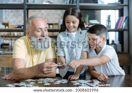 Help is what really matters. Selective focus on hands of a retired gentleman and his grandkids smiling and chatting while working on a puzzle picture together.