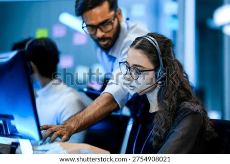 IT helpdesk specialist resolving technical software issues via voip headset. Senior supervisor mentoring support agent on crm interface.