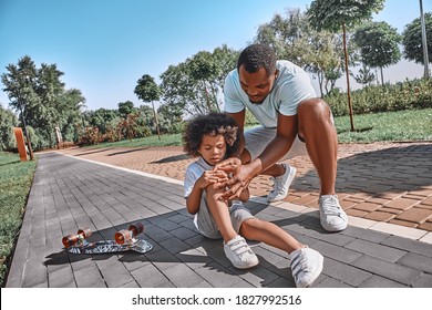 Helpful Afro-American Dad Checking His Kid Minor Injury After A Fall From A Skateboard