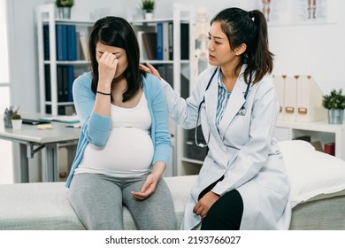 Helpful Asian Female Psychologist Doctor Is Comforting And Patting On The Back Of The Sad Expectant Mom Who’s Covering Her Face On The Treatment Bed In Hospital