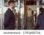 Helpful doorman wearing uniform welcoming people inside the hotel while holding the entrance door open