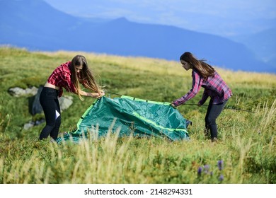 Helpful to have partner for raising tent. Camping skills concept. In middle of nowhere. Girls set up tent on top of mountain. Camping and hiking. Summer adventures. Temporary housing. Camping trip