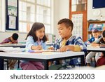 Helpful school girl assisting classmate in studies at elementary school. Two friends studying together in classroom in primary school. Middle eastern girl helping schoolboy in homework or schoolwork. 